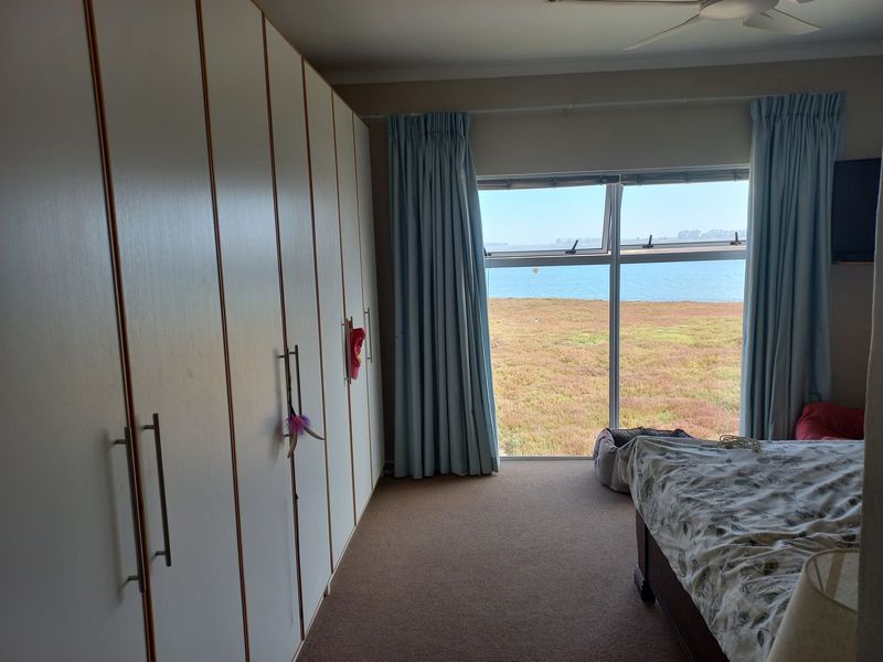A bedroom featuring extensive built-in cupboards, a ceiling fan, and a large window offering scenic water views.