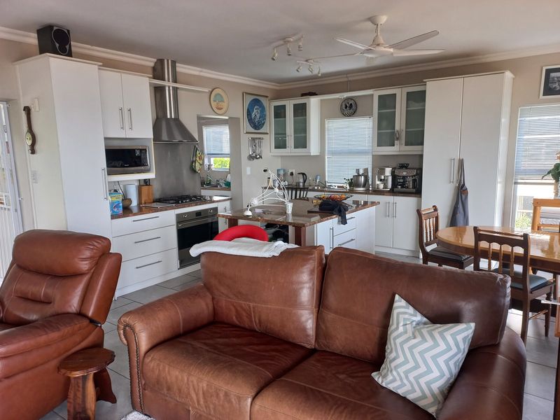 Spacious open-plan kitchen and living area featuring modern white cabinetry, stone countertops, built-in appliances, and tiled flooring throughout.