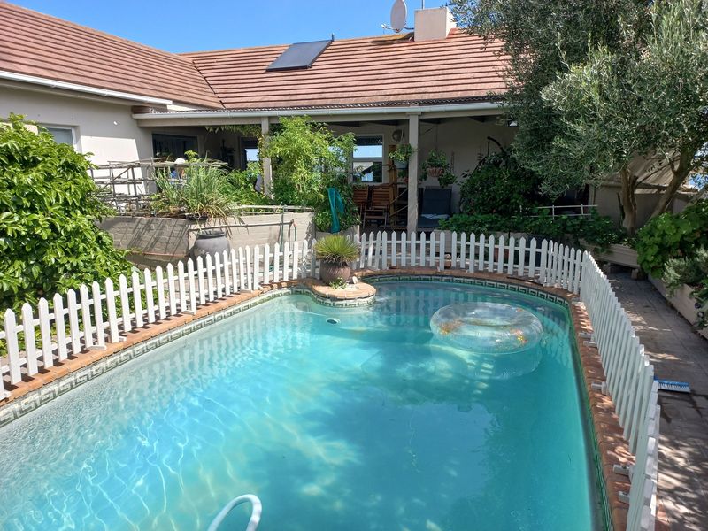 Outdoor pool area featuring a swimming pool with safety fencing, adjacent to a covered patio and the main house structure with a tiled roof.