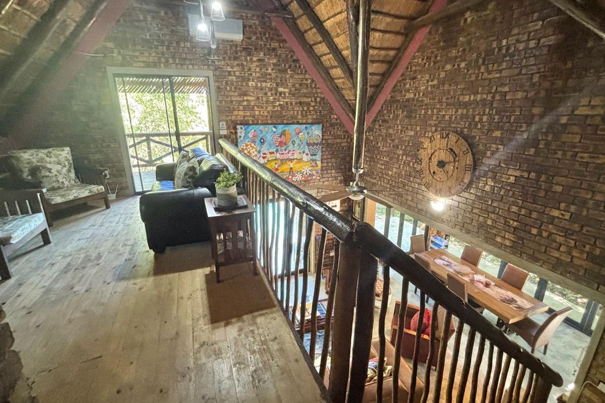 A rustic mezzanine living area featuring exposed brick walls, a traditional thatched roof, and timber flooring overlooking the main living space below.