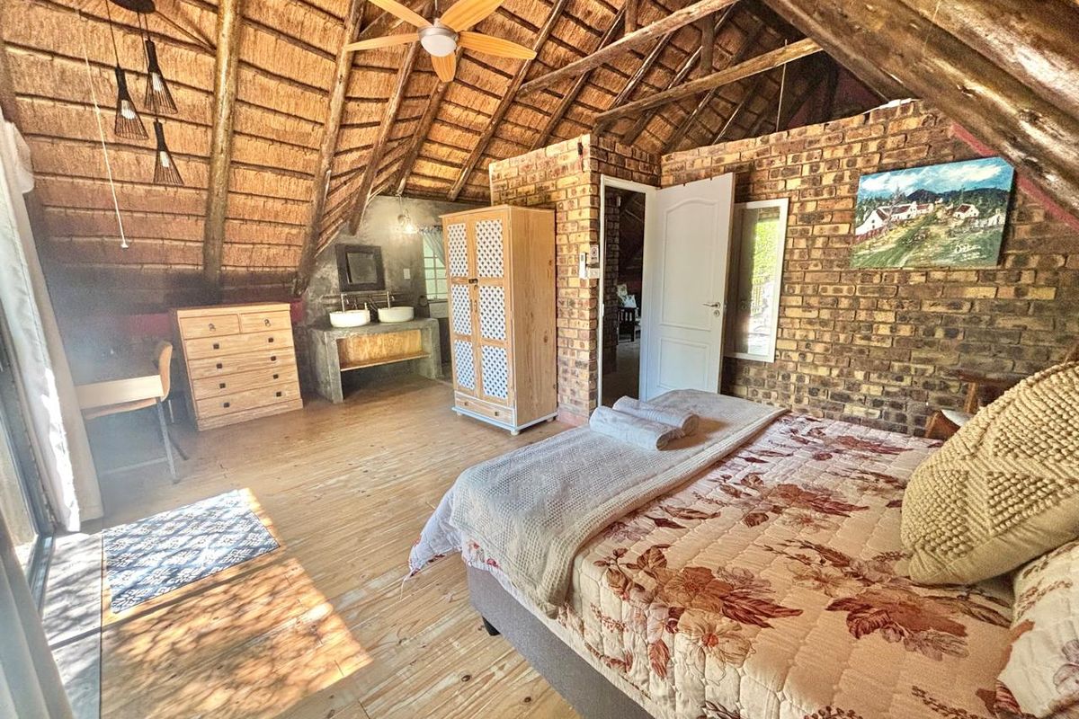 Spacious bedroom featuring an exposed thatch roof, timber flooring, and rustic brick walls with an integrated double vanity area.