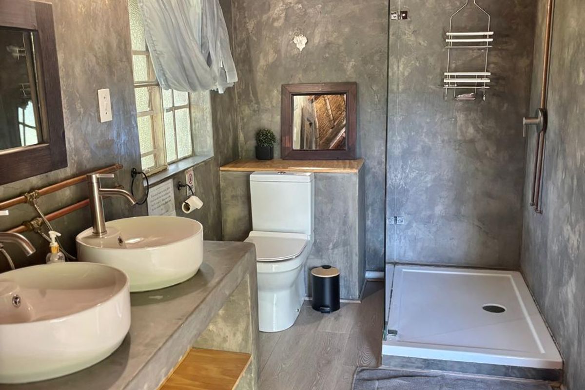 A rustic-style bathroom featuring a double vanity with vessel sinks, exposed copper plumbing, a walk-in shower, and a unique exposed thatch roof.