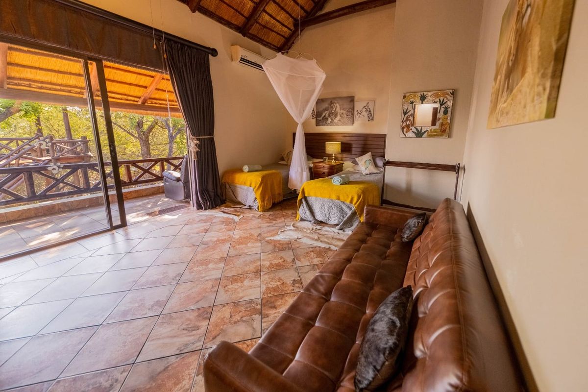 Spacious bedroom featuring a high thatched ceiling with exposed rafters, tiled flooring, and direct access to a private timber deck through sliding glass doors.