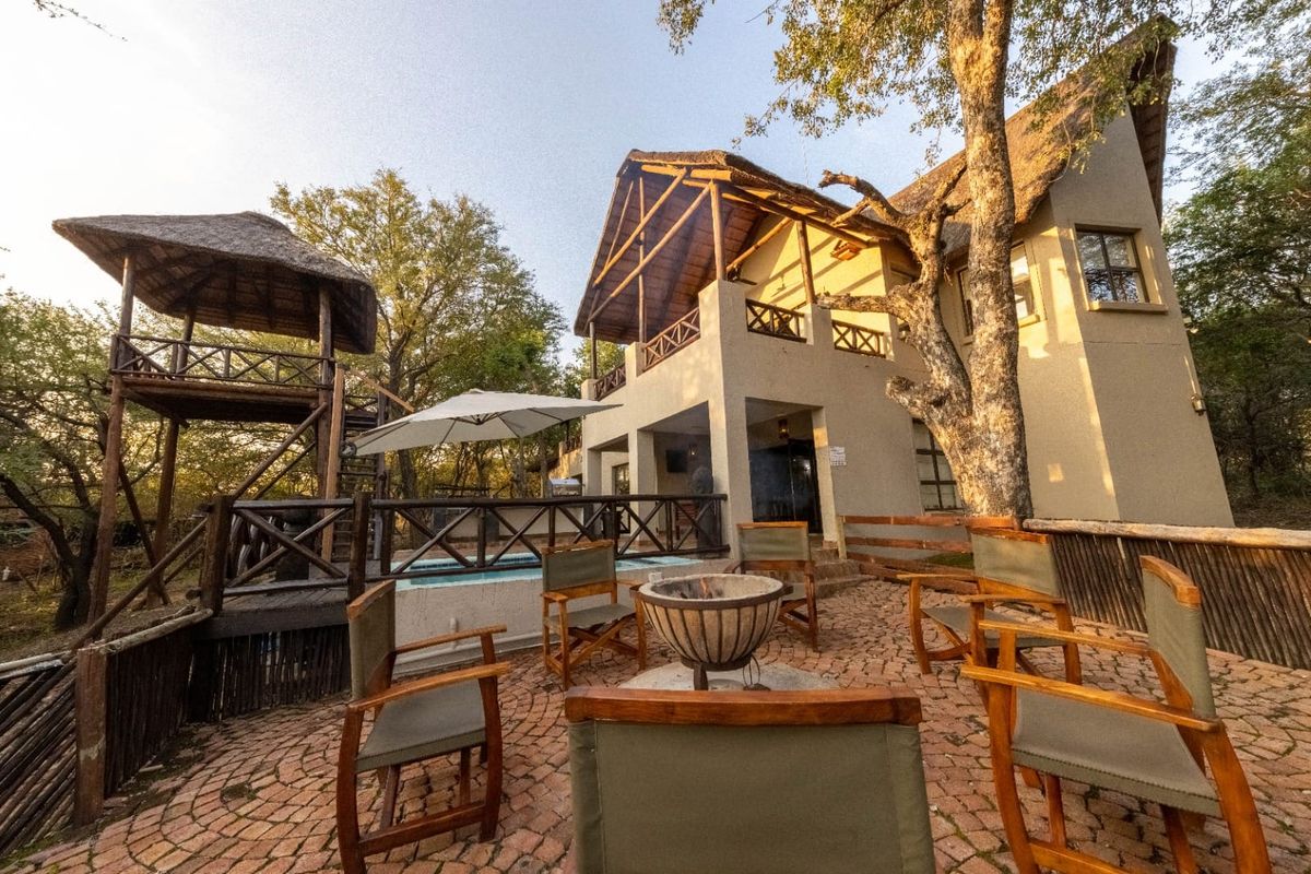 Rear exterior view featuring a thatched roof house, a paved boma fire pit area, a plunge pool, and a raised wooden deck.