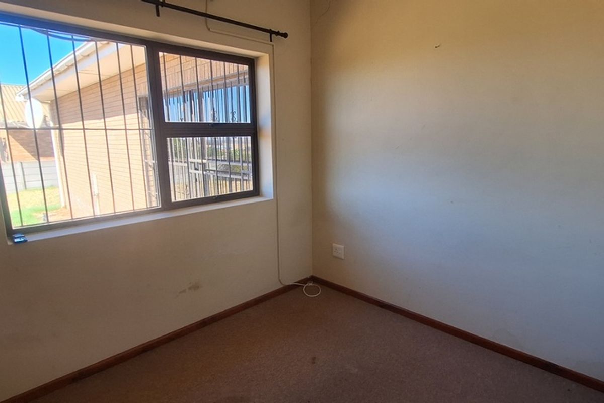 A vacant bedroom featuring a window with security bars and carpeted flooring, offering a blank canvas for potential updates.