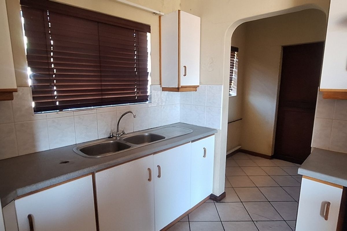 A functional kitchen featuring white cabinetry, tiled splashbacks, a double-basin sink, and integrated cooktop, offering a practical layout for daily meal preparation.