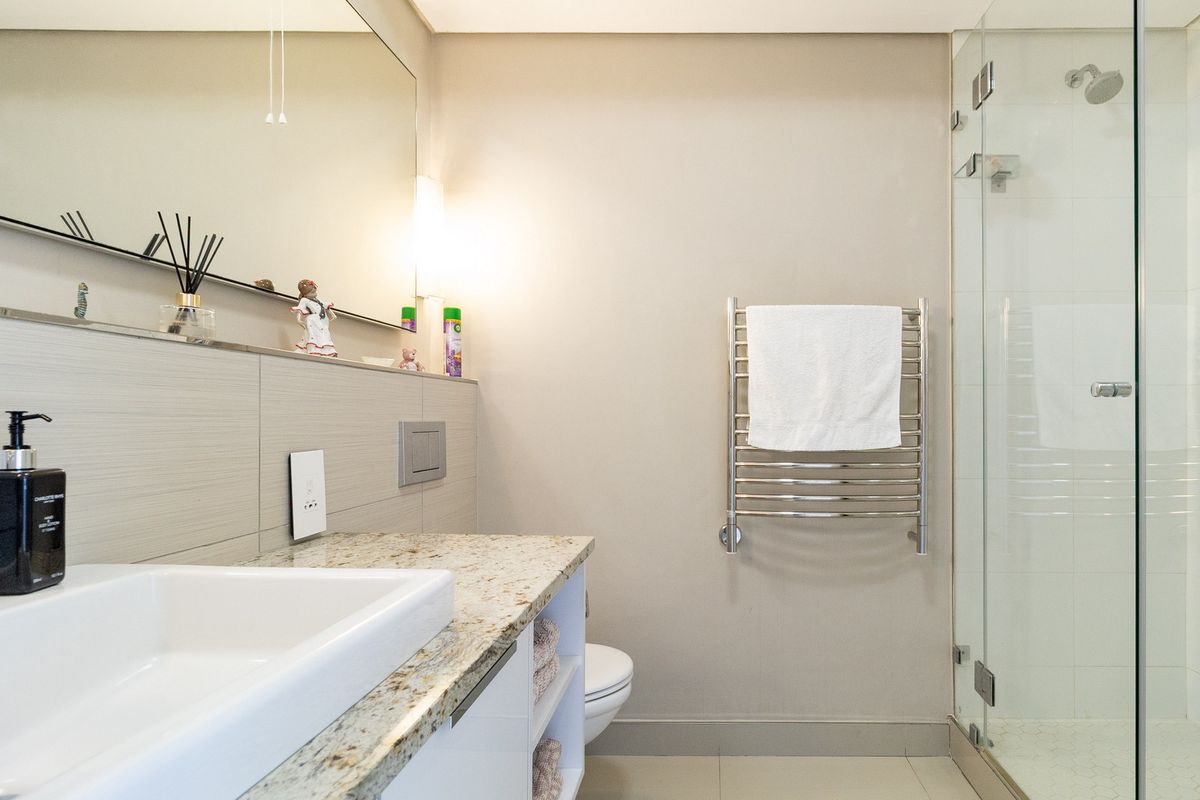 Modern bathroom featuring a granite vanity, glass-enclosed shower, and a heated towel rail, finished with neutral wall tones and tiled surfaces.