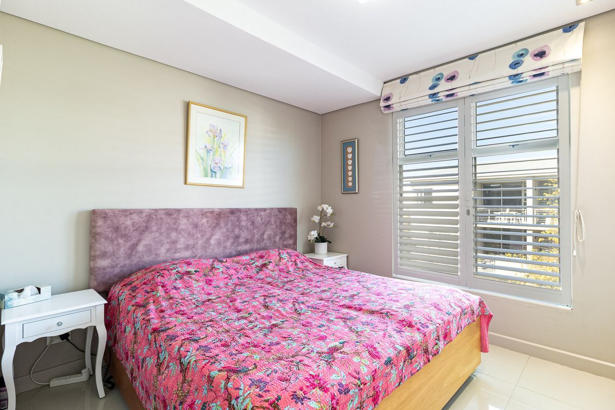 A well-maintained bedroom featuring tiled flooring, fitted window shutters, and a clean, neutral aesthetic.