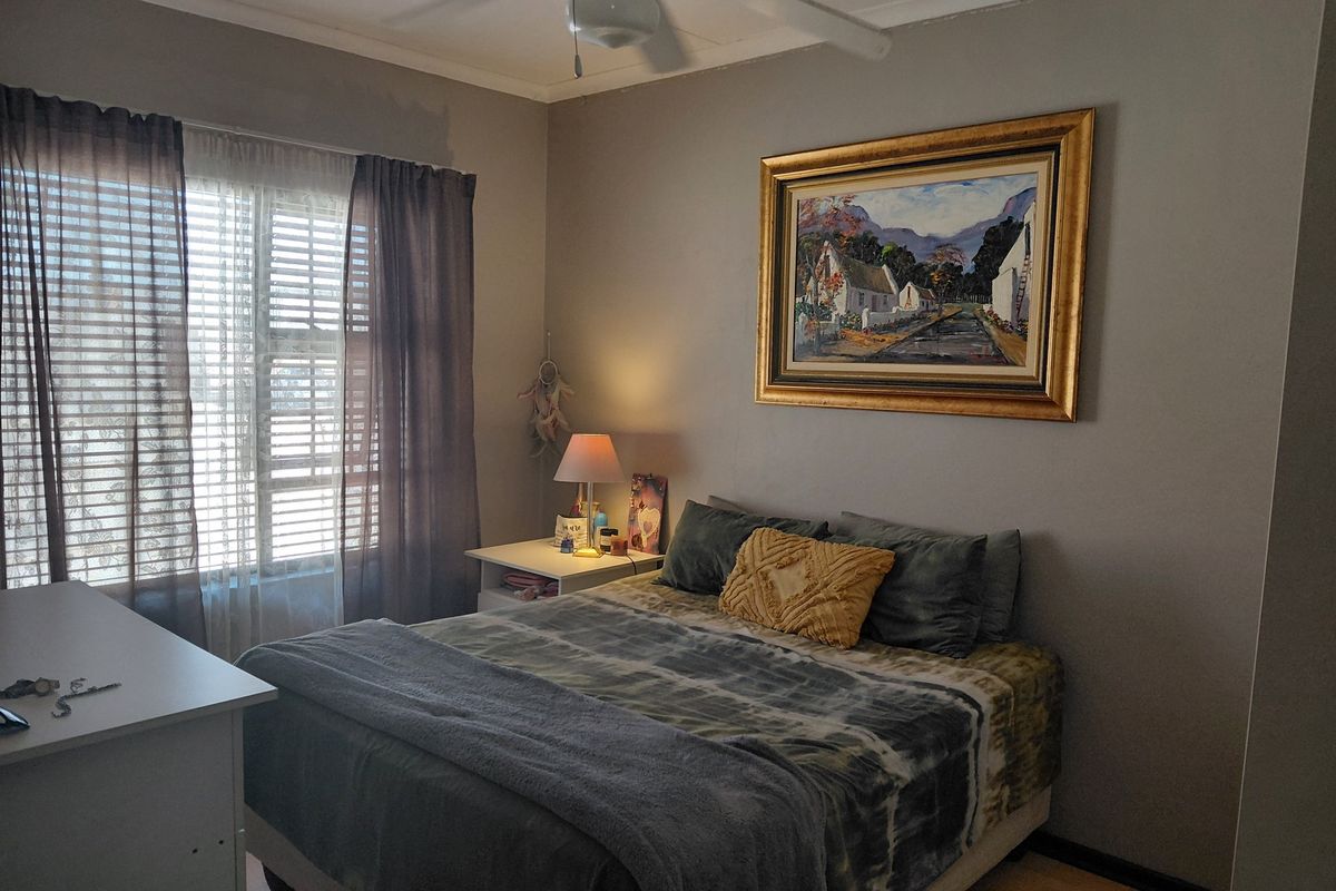 A cozy bedroom featuring a ceiling fan, laminate flooring, and large window with blinds, providing a comfortable and functional living space.