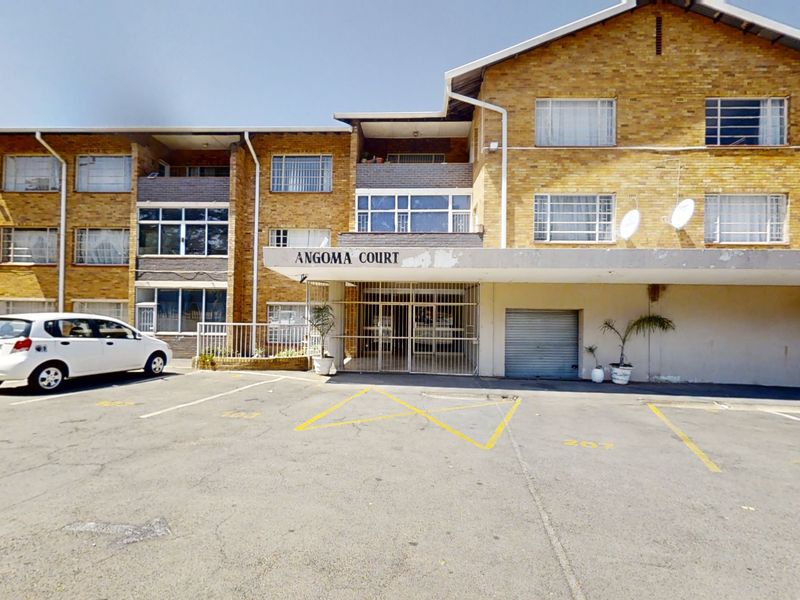 Front elevation of Angoma Court apartment building featuring a brick facade, concrete entrance canopy, and dedicated asphalt parking bays.