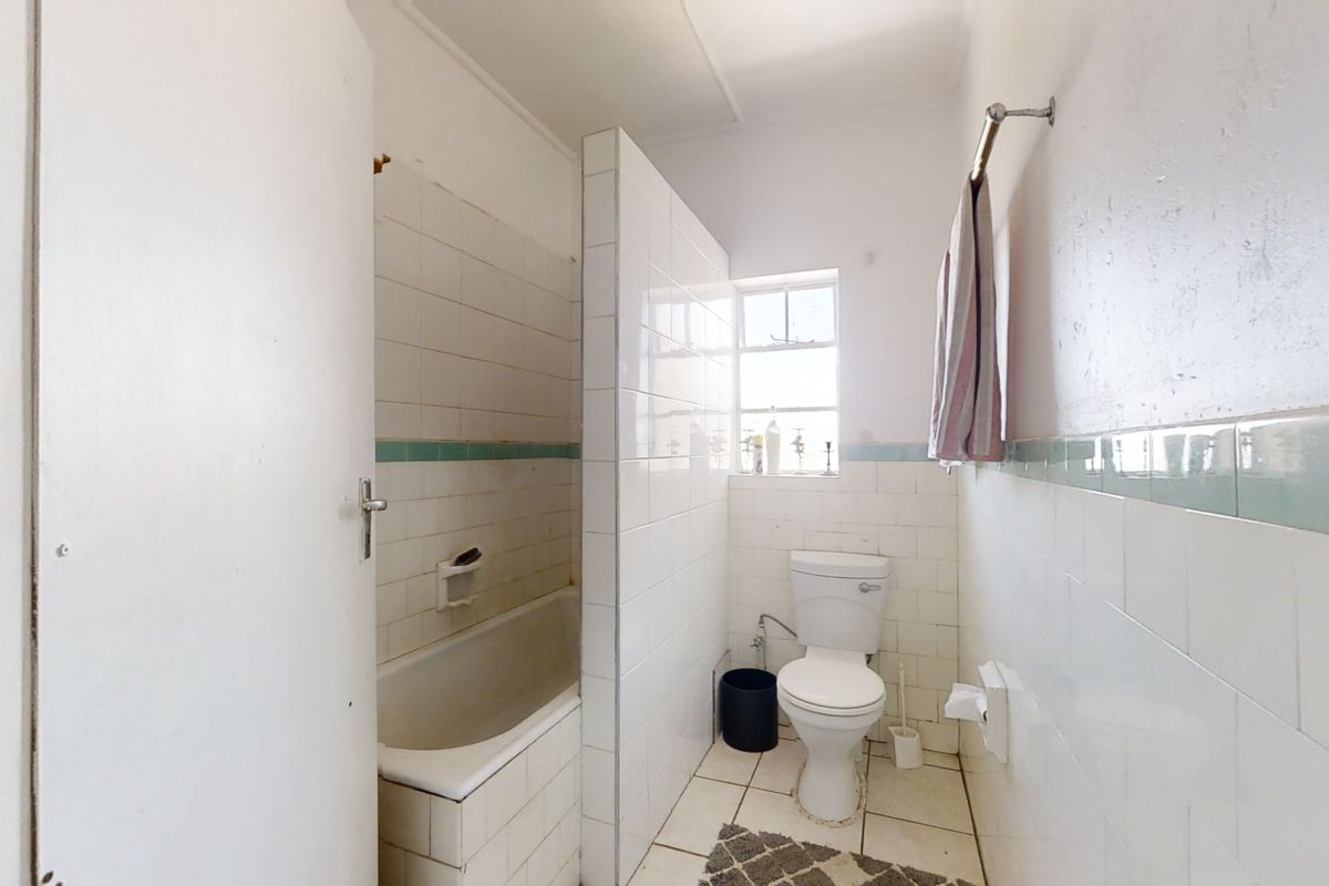 A dated bathroom featuring a built-in bathtub, toilet, and tiled finishes, requiring cosmetic updates to modernize the space.