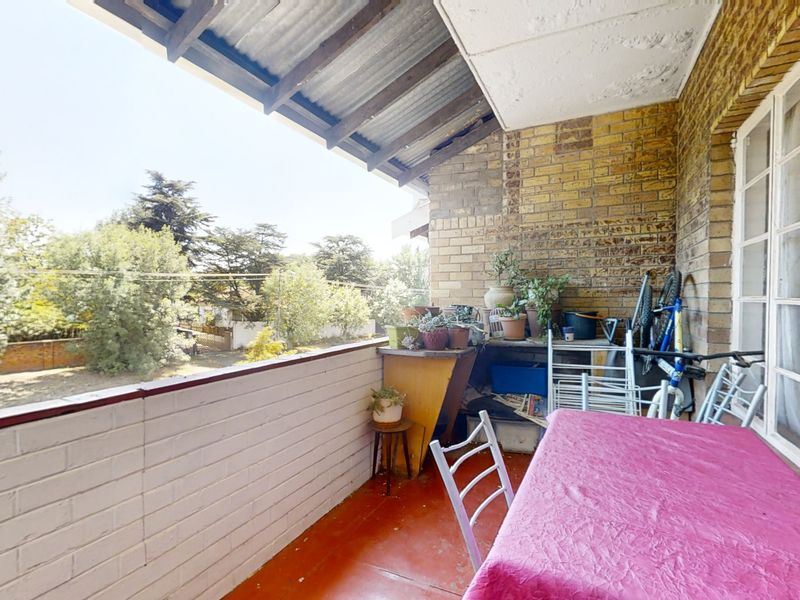 A covered balcony featuring exposed brick walls, a corrugated metal roof, and a painted brick balustrade, offering an outdoor space with garden views.