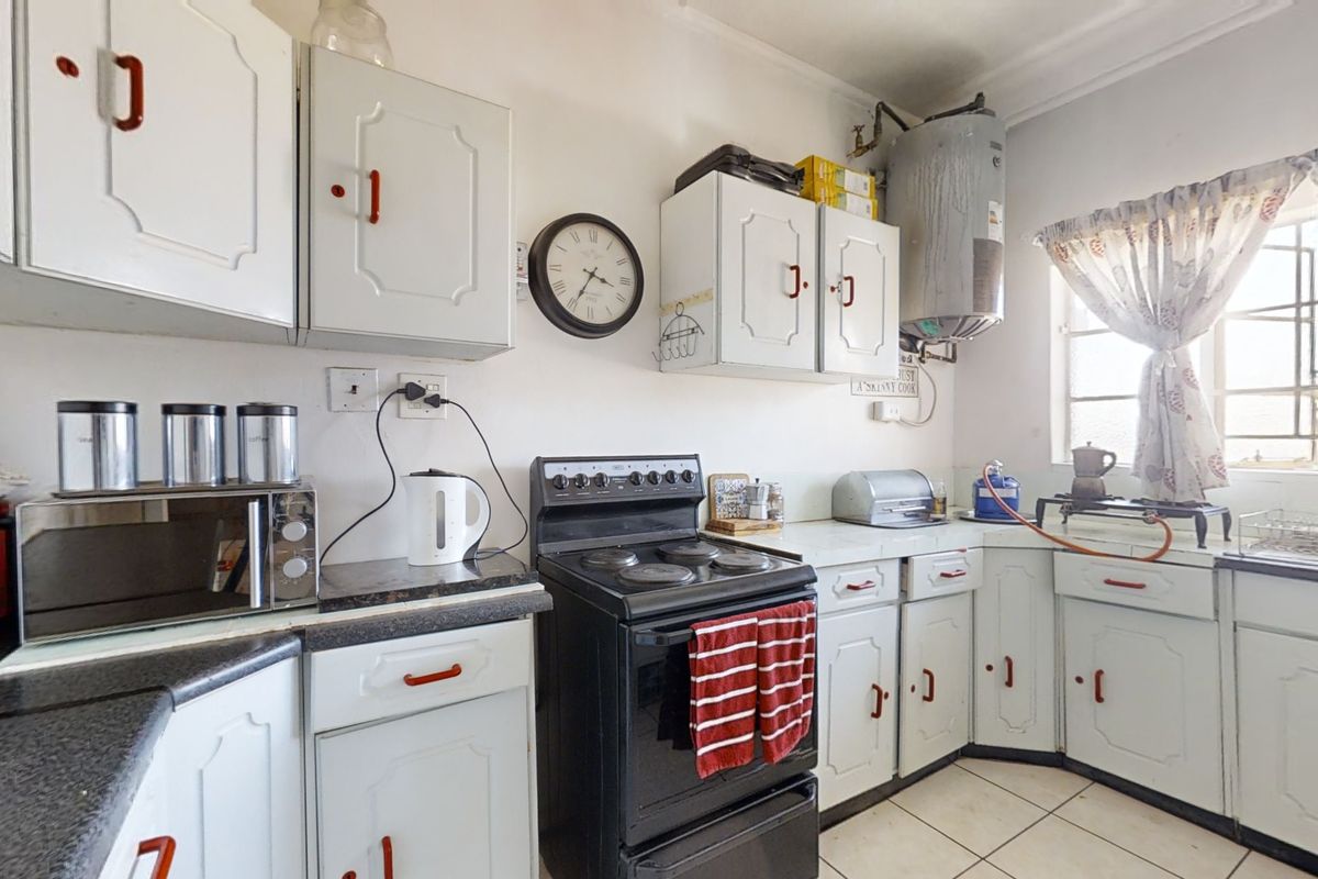A functional kitchen featuring white cabinetry, dark laminate countertops, an electric stove, and an exposed wall-mounted water heater.