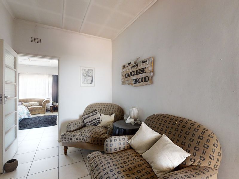 A living area featuring tiled flooring and a panelled ceiling, providing access to an adjacent bedroom.