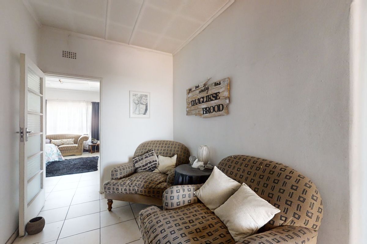 A living area featuring tiled flooring and a panelled ceiling, providing access to an adjacent bedroom.