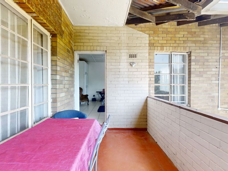 A covered balcony featuring exposed brick walls, tiled flooring, and steel-framed windows, offering an outdoor space with potential for modernization.