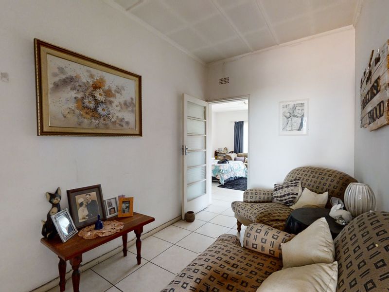 A living room area featuring tiled flooring and a panelled ceiling, with an internal door leading to an adjacent bedroom.