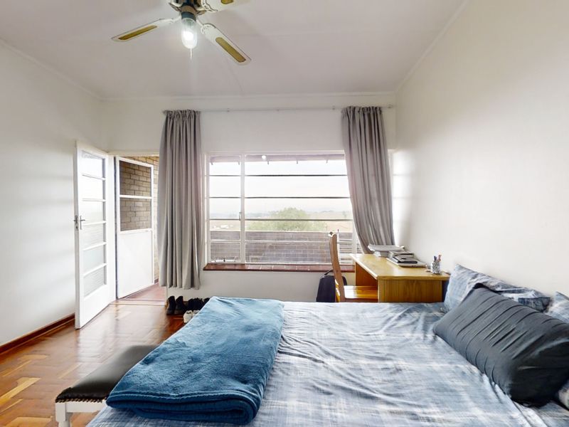 A bedroom featuring parquet flooring, a ceiling fan, and direct access to an outdoor balcony through a glass panel door.
