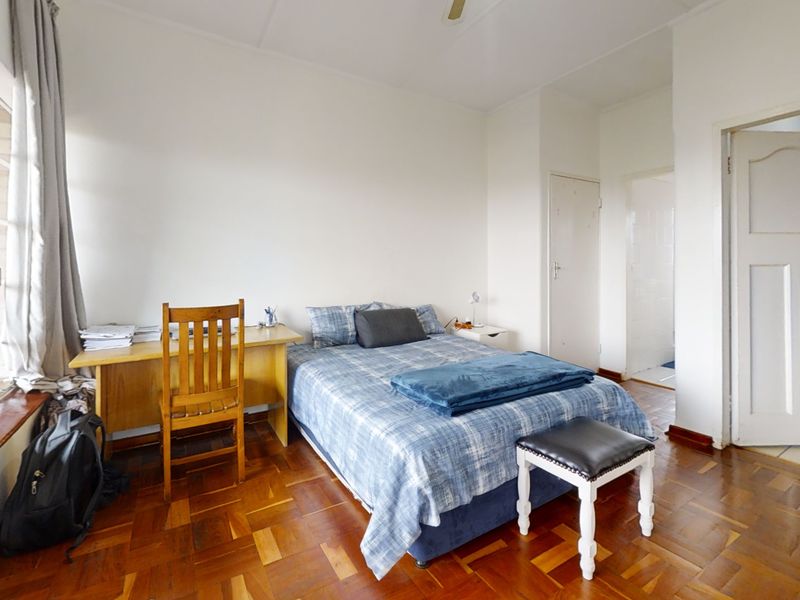 A bedroom featuring classic parquet flooring, a large window providing natural light, and a ceiling fan.