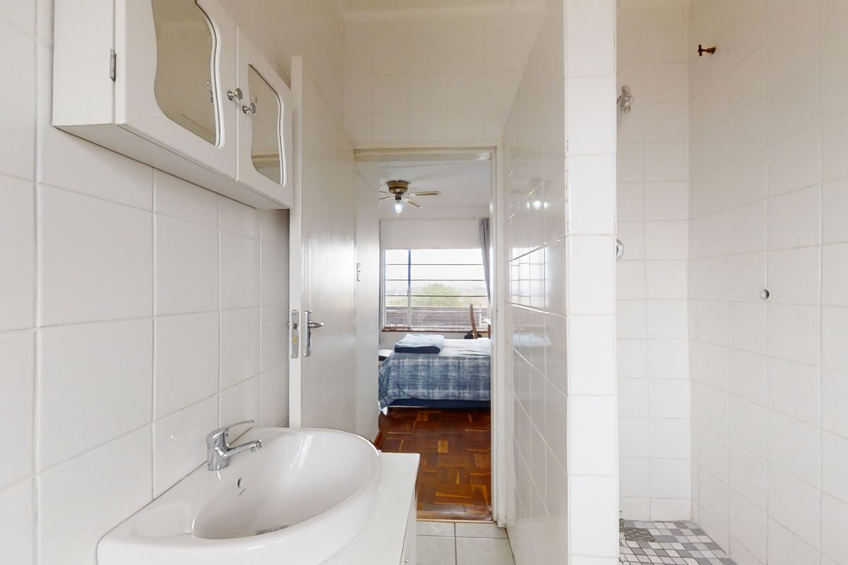 A functional bathroom featuring a wall-mounted vanity, ceramic basin, and a tiled shower enclosure, with a view into the adjacent bedroom.