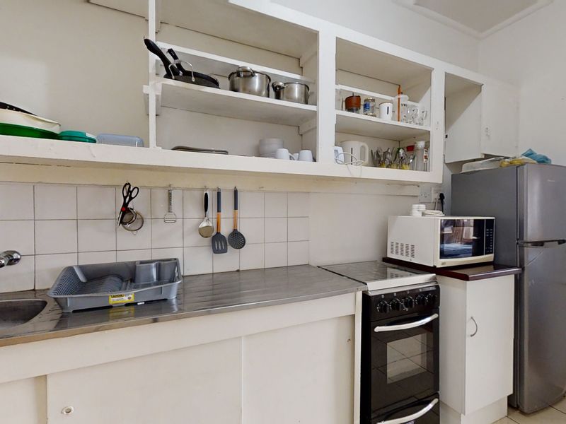 A functional kitchen featuring stainless steel sink, tiled splashback, freestanding oven, and open shelving with built-in cabinetry.