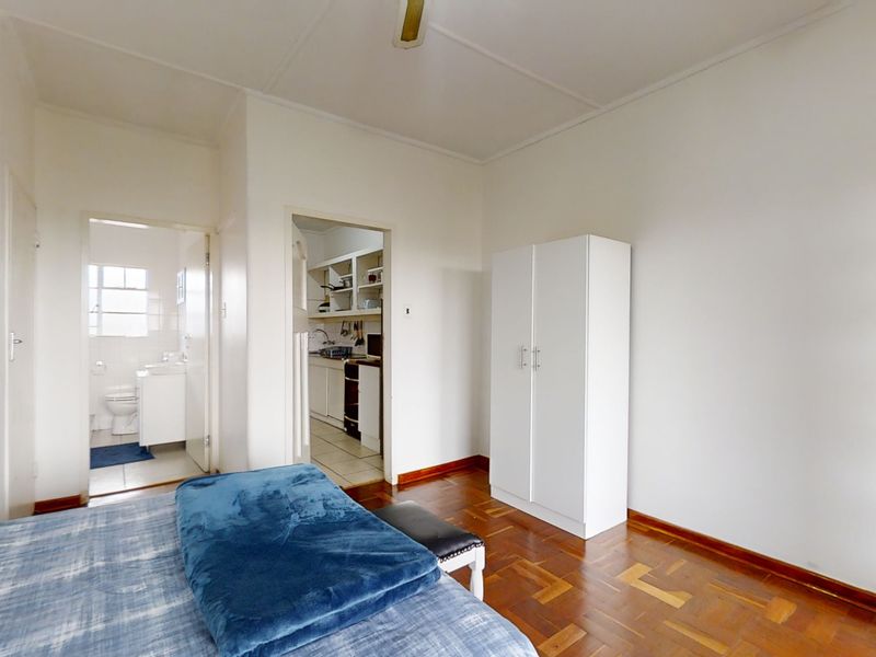 Bedroom featuring parquet flooring, a ceiling fan, and a built-in wardrobe, with direct access to an adjoining bathroom and kitchen area.