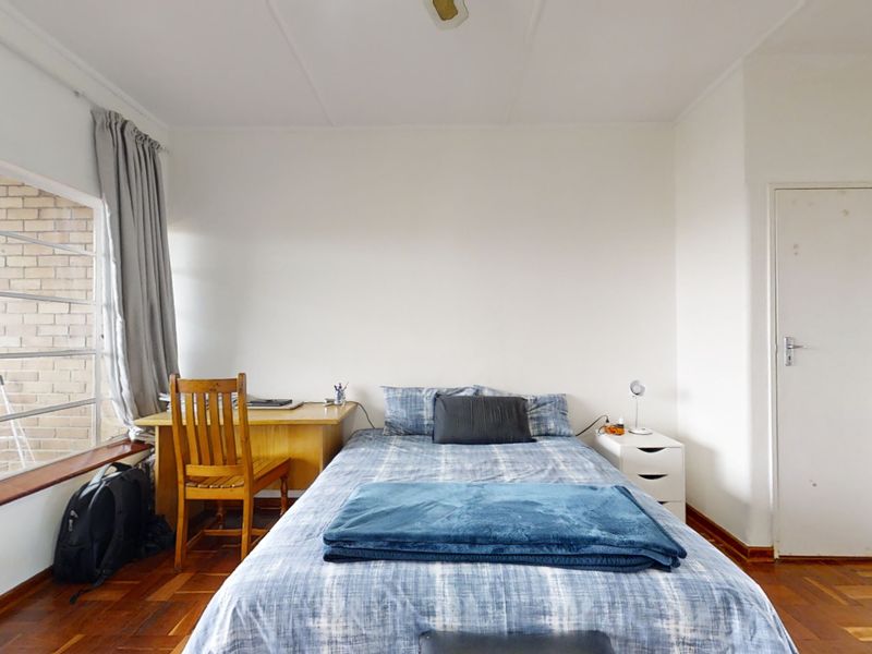 A bedroom featuring classic parquet flooring, a large window providing natural light, and a standard internal door.