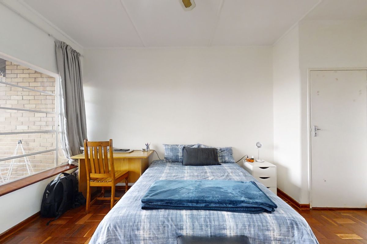 A bedroom featuring classic parquet flooring, a large window providing natural light, and a standard internal door.
