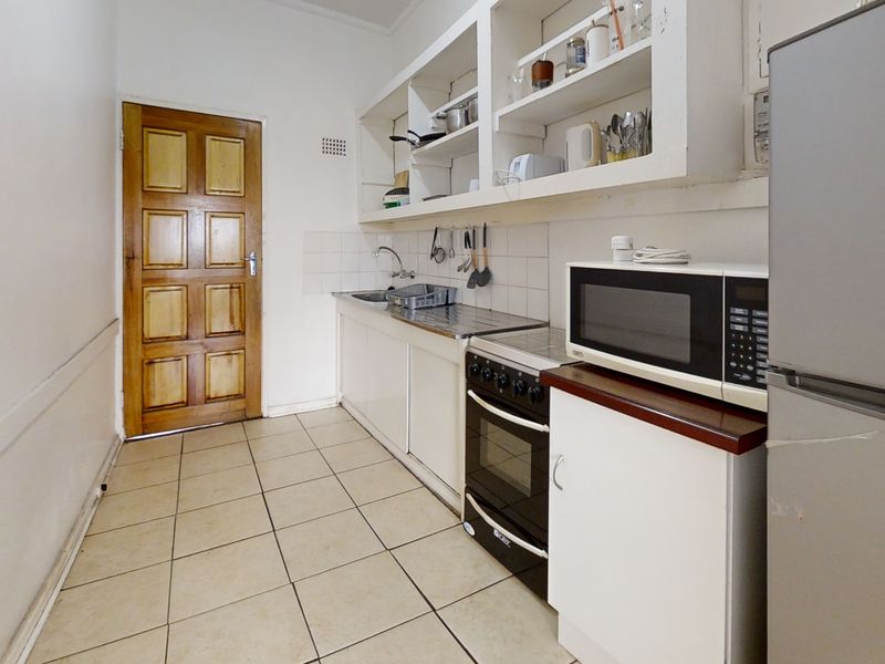 A compact kitchen featuring basic cabinetry, open shelving, a stainless steel sink, and a freestanding oven, with tiled flooring throughout.