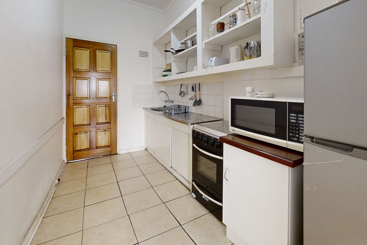 A compact kitchen featuring basic cabinetry, open shelving, a stainless steel sink, and a freestanding oven, with tiled flooring throughout.