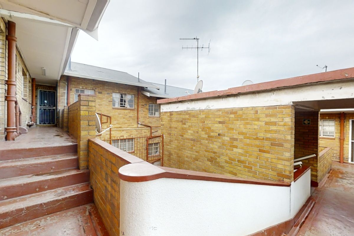 Exterior view of the flat complex featuring brick facade, concrete staircases, and security gates in a functional, dated condition.
