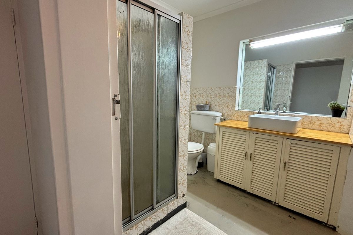 A functional bathroom featuring a shower enclosure, a vessel sink set on a wooden vanity, and a wall-mounted mirror.