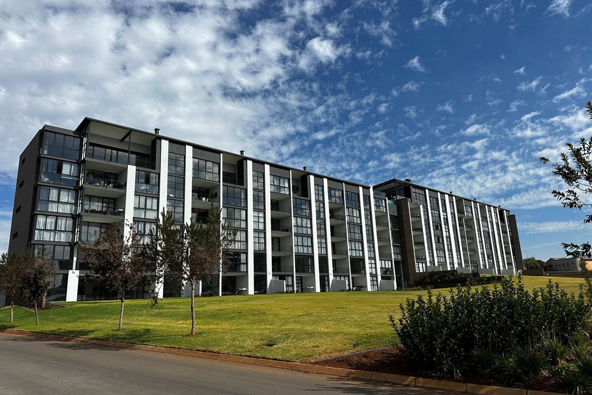 A modern multi-story apartment complex featuring a contemporary facade with large glass windows and balconies, set against a well-maintained landscaped lawn.