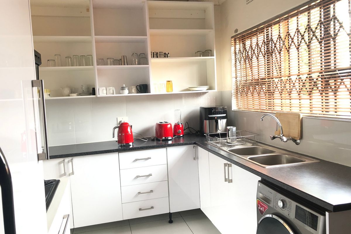 Modern kitchen featuring white cabinetry, dark countertops, double stainless steel sink, and integrated laundry appliance space.