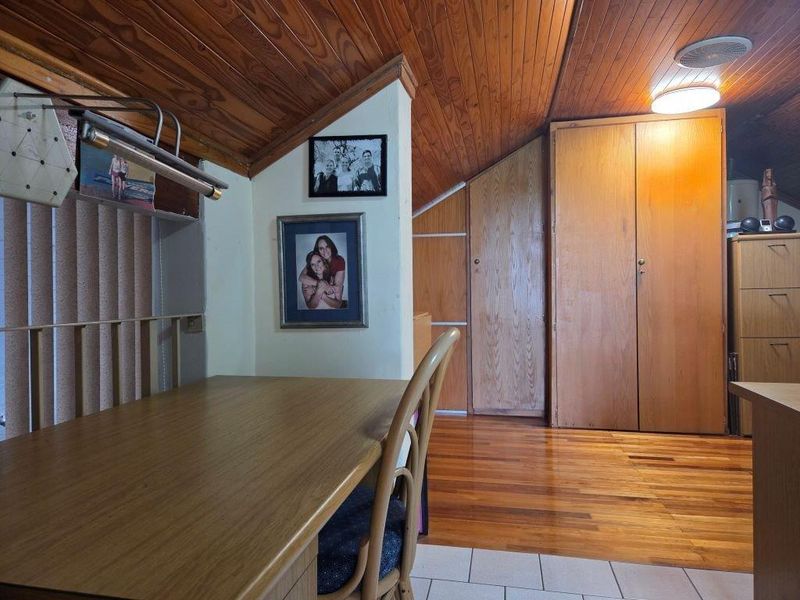 A bedroom featuring a vaulted timber-clad ceiling, built-in timber wardrobes, and a combination of hardwood and tiled flooring.