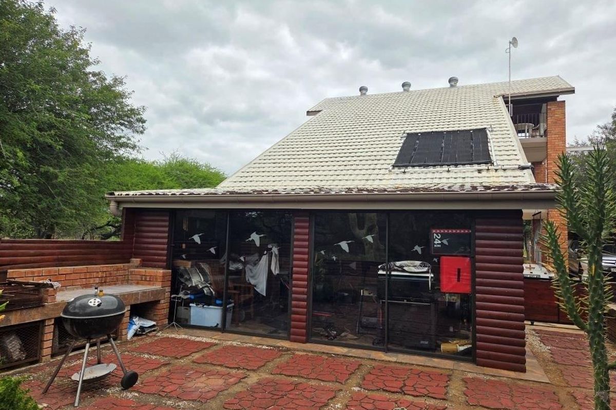 Rear exterior view featuring a paved patio, built-in brick braai, and sliding glass doors leading into the home, with solar panels installed on the roof.