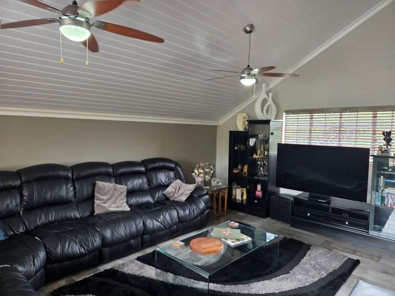 A comfortable living room featuring a vaulted tongue and groove ceiling with dual ceiling fans and large windows with venetian blinds.