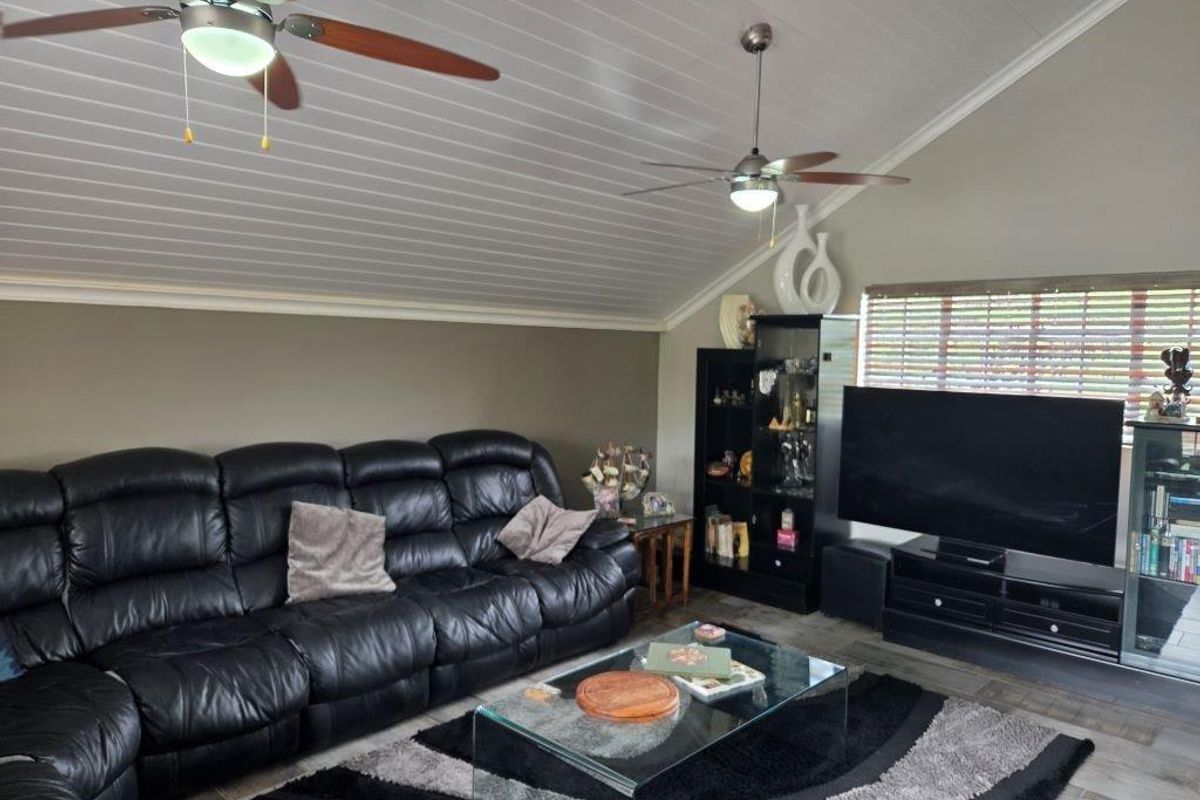 A comfortable living room featuring a vaulted tongue and groove ceiling with dual ceiling fans and large windows with venetian blinds.