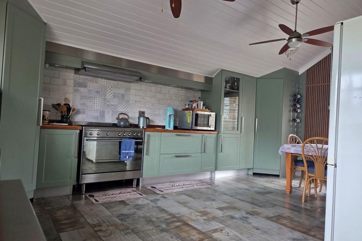 A well-maintained kitchen featuring sage green cabinetry, timber countertops, a tiled backsplash, and dual ceiling fans, offering a functional and stylish cooking space.