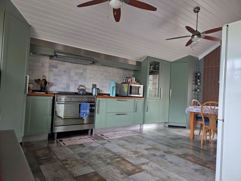 A well-maintained kitchen featuring sage green cabinetry, timber countertops, a tiled backsplash, and dual ceiling fans, offering a functional and stylish cooking space.
