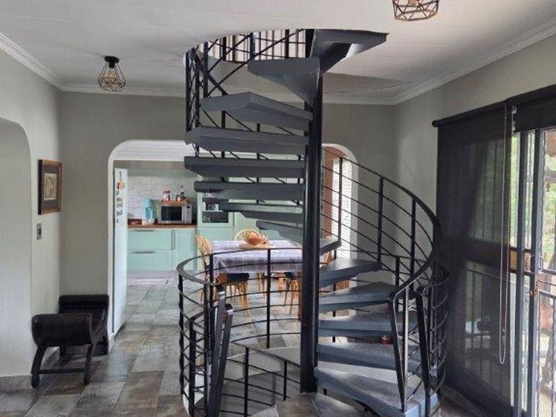 A living area featuring a prominent black metal spiral staircase, wood-look tiled flooring, and sliding glass doors leading to the exterior.