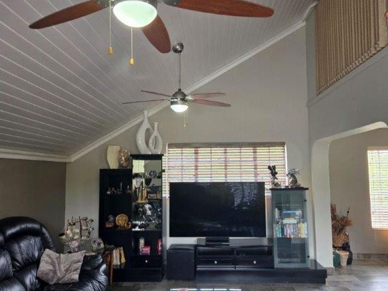 Spacious living room featuring a high vaulted tongue and groove ceiling, dual ceiling fans, and tiled flooring with an open archway leading to adjacent areas.