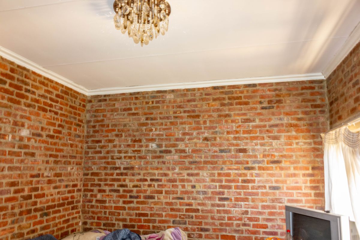 A bedroom featuring rustic exposed brick walls, decorative crown molding, and a classic crystal chandelier, offering a warm and textured aesthetic.
