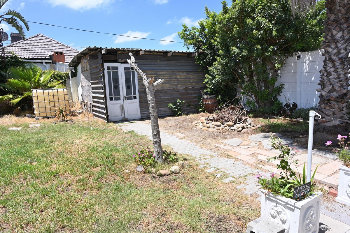 Rear garden area featuring a corrugated metal shed, paved pathway, and stone fire pit, requiring landscaping and structural maintenance.