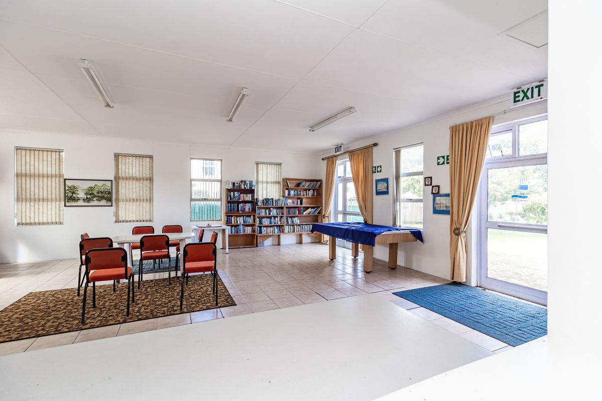 A spacious multi-purpose room featuring tiled flooring, large windows with vertical blinds, and multiple glass-paneled exit doors leading to the exterior.