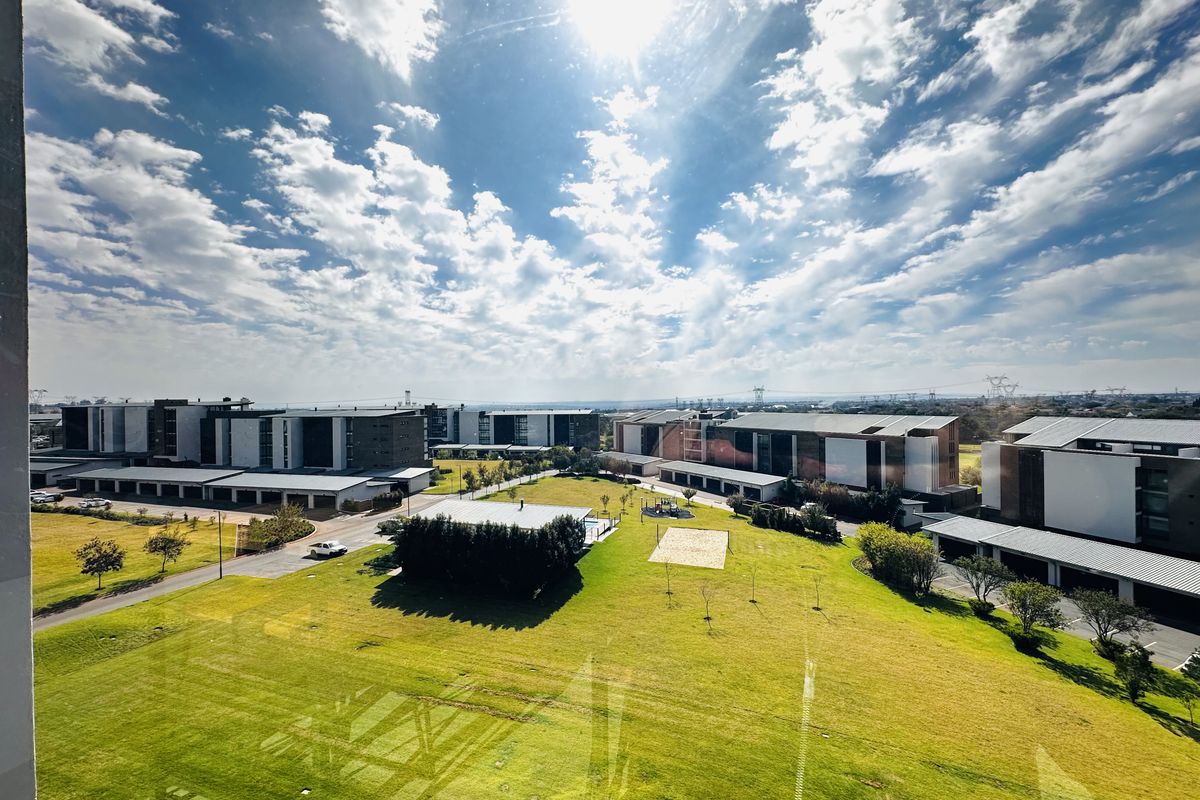 Elevated aerial view overlooking the apartment complex grounds, featuring landscaped lawns, communal pathways, and surrounding residential buildings.