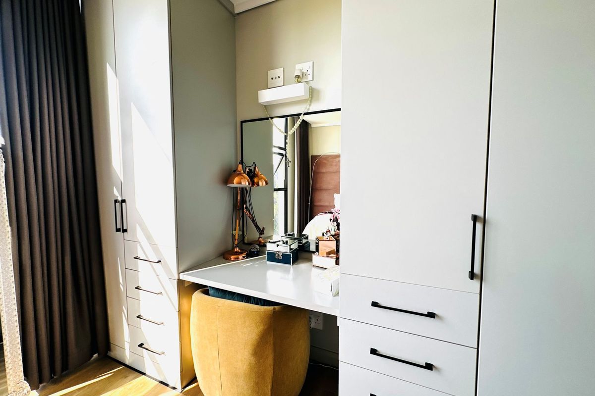 A well-appointed bedroom featuring custom built-in floor-to-ceiling wardrobes with integrated vanity desk and mirror.