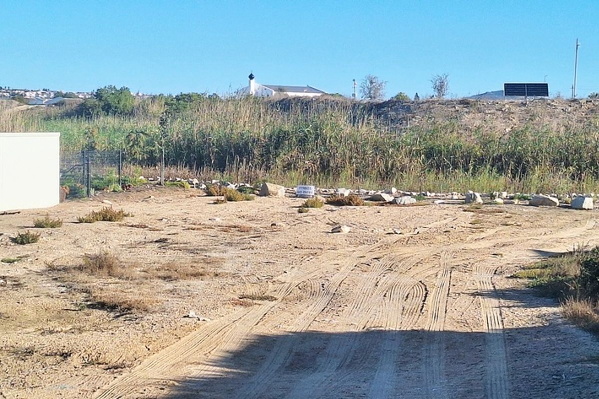 A vacant residential plot featuring sandy terrain, natural vegetation, and boundary walling, offering a blank canvas for future development.