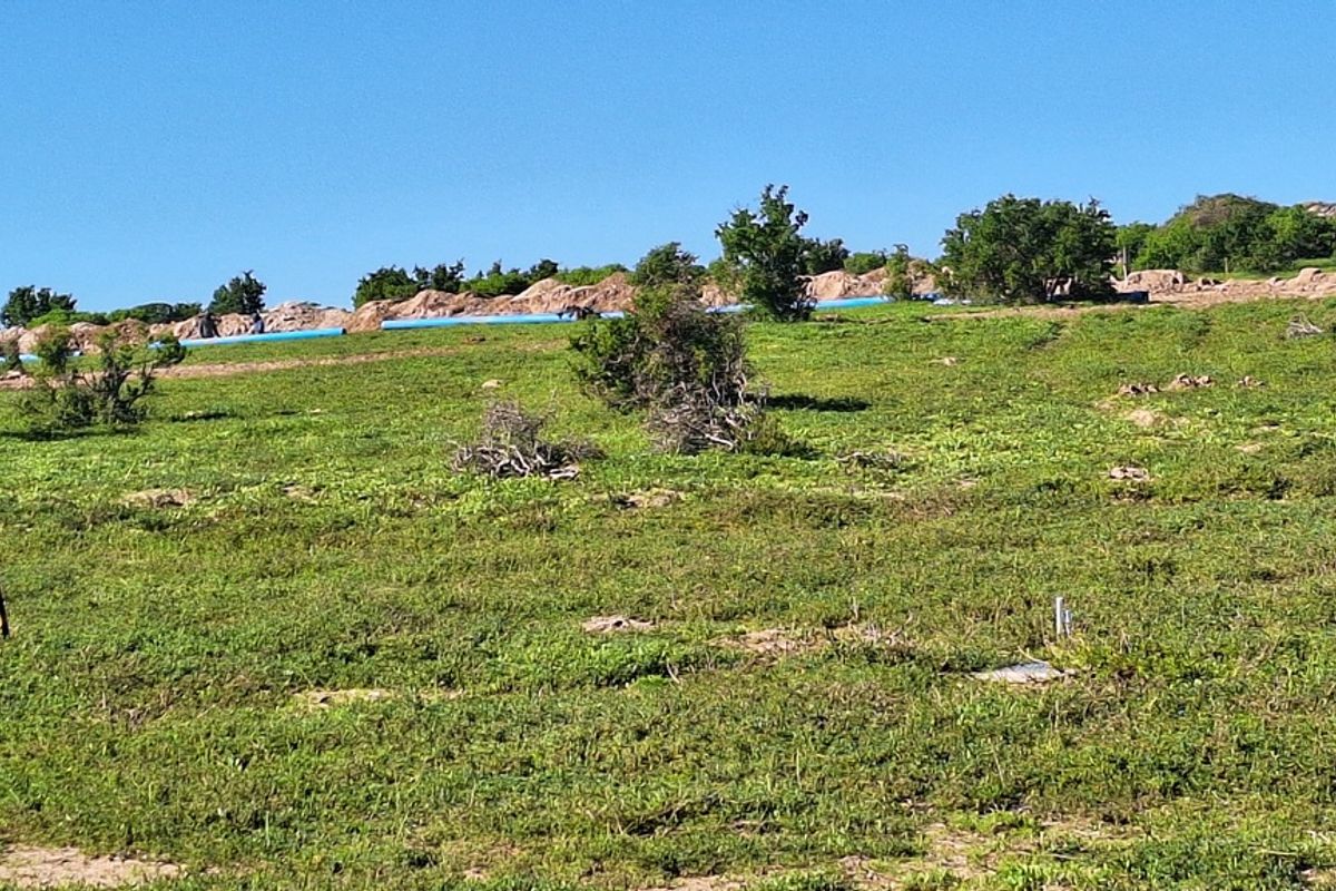 A view of a vacant residential plot featuring natural vegetation, open terrain, and visible utility piping across the landscape.