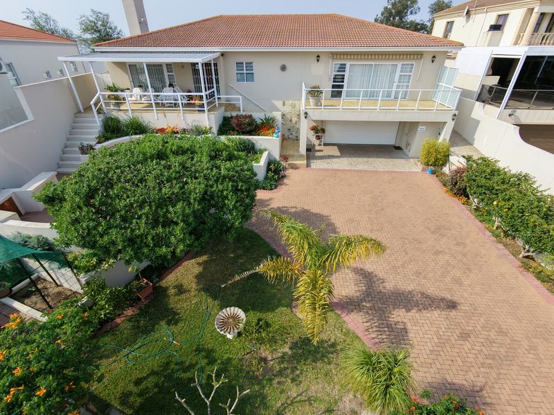 Rear view of a multi-level house featuring a paved driveway, double garage, elevated balcony, and a covered patio overlooking a landscaped garden.